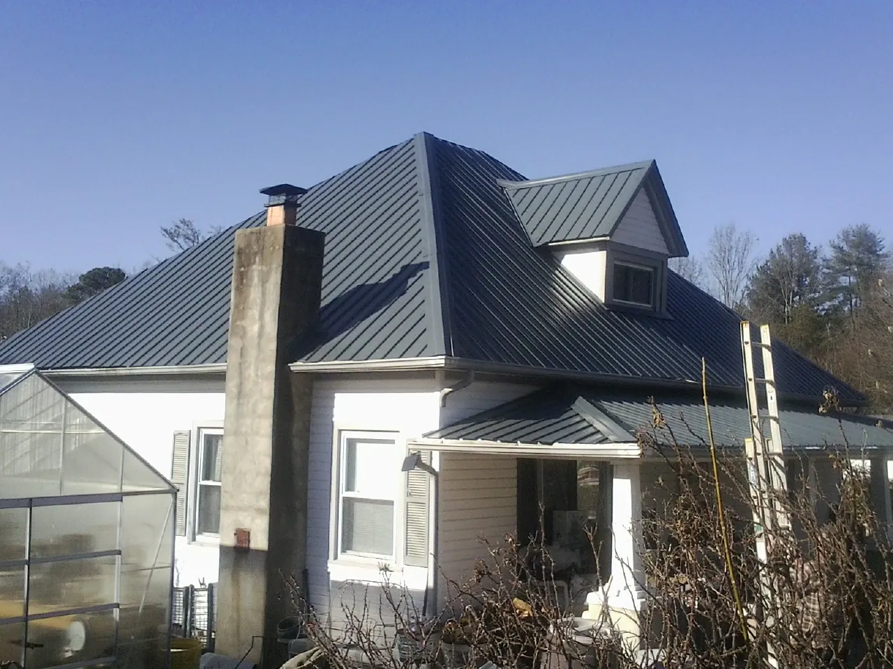 Dark blue standing seam metal roof on a white farmhouse with dormer — Slate & Tile Roof Repair by Roofing Brothers in Harshaw