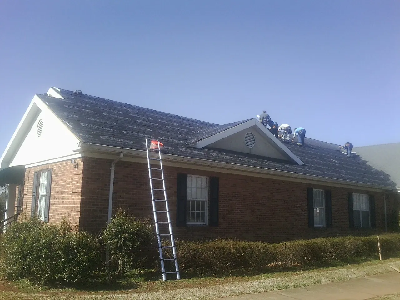 Crew tearing shingles off a brick ranch roof with a ladder set — Emergency Roof Repair work by our crew in Harshaw