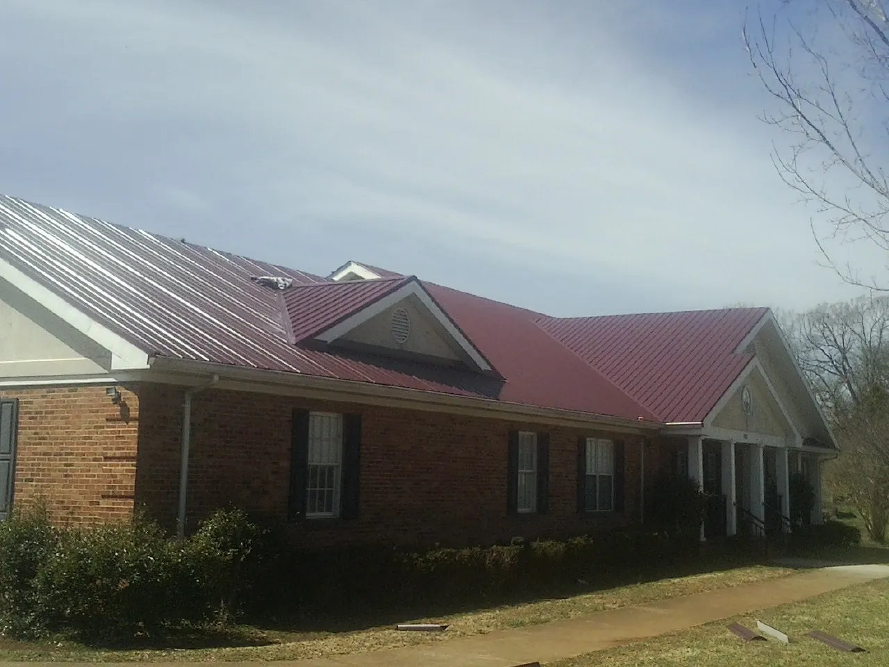 Red metal roof with gabled entries on a long brick building, from a Hail Damage Roof Repair job in Harshaw