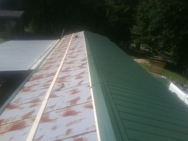Old rusted panels beside newly installed green metal roofing — Wind Damage Roof Repair by Roofing Brothers in Harshaw