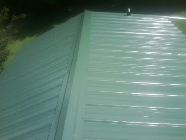 New green metal panels meeting at the ridge of a roof — Flat Roof Repair work by our crew in Harshaw