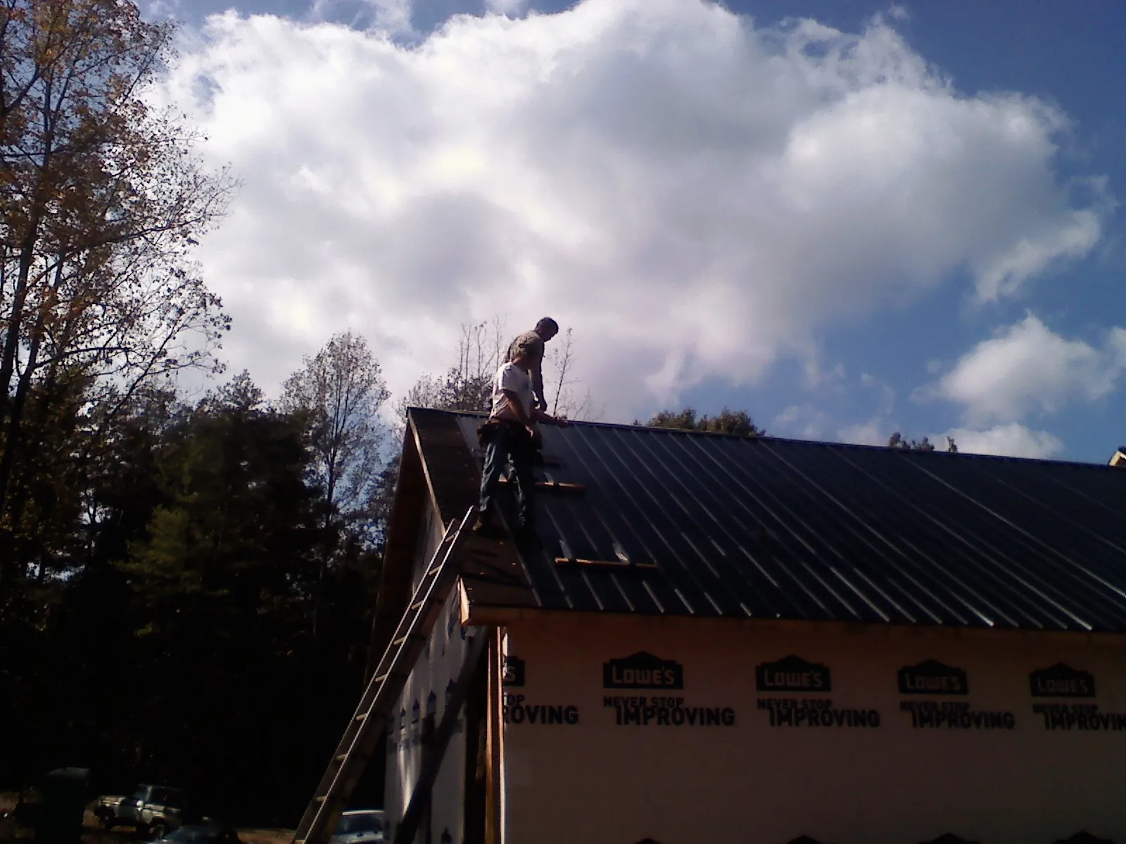 Roofer fastening dark metal panels high against a cloudy sky, from a Roof Inspection job in Harshaw