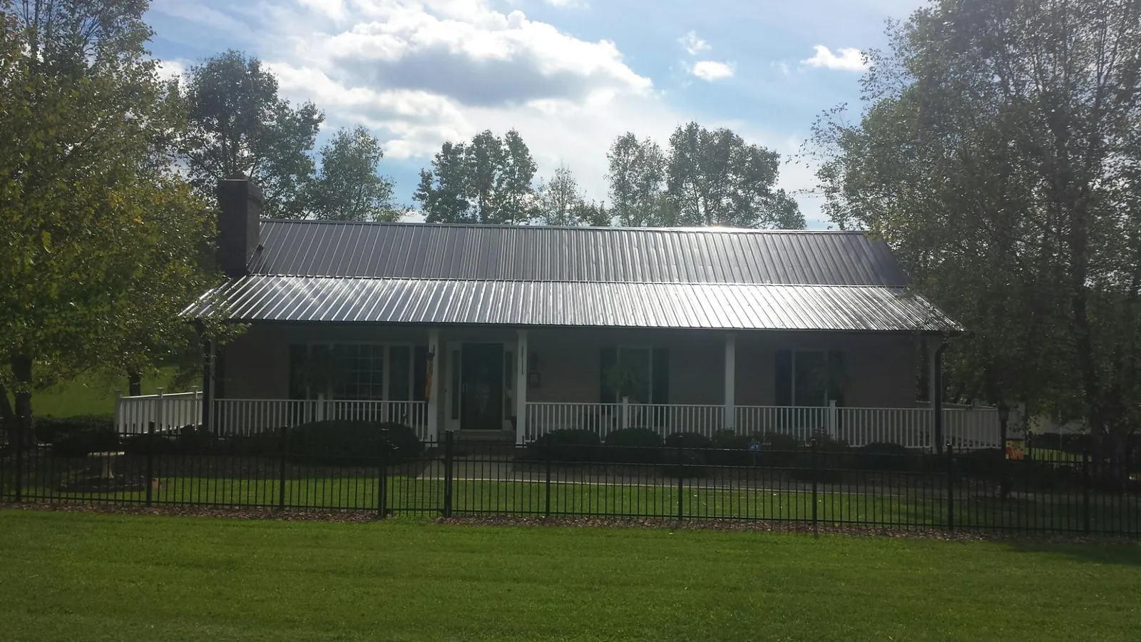Gray metal roof on a brick ranch with a full width front porch — Gutter Guard Installation work by our crew in Harshaw