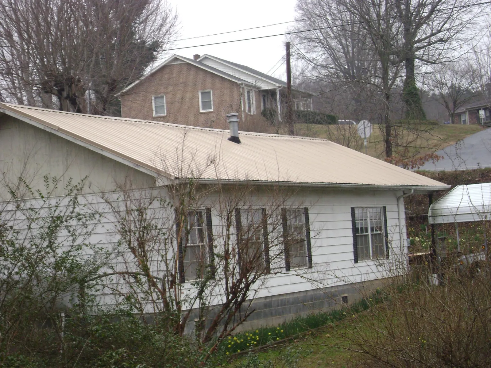 Tan metal roof on a white sided house set into a hillside — Commercial Roofing by Roofing Brothers in Harshaw